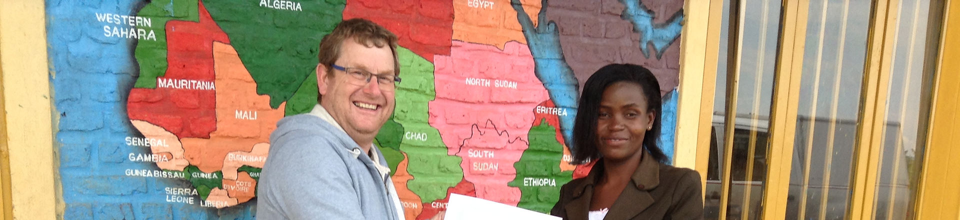A man, Robert Astick, shaking hands with a woman in front of a map of Africa